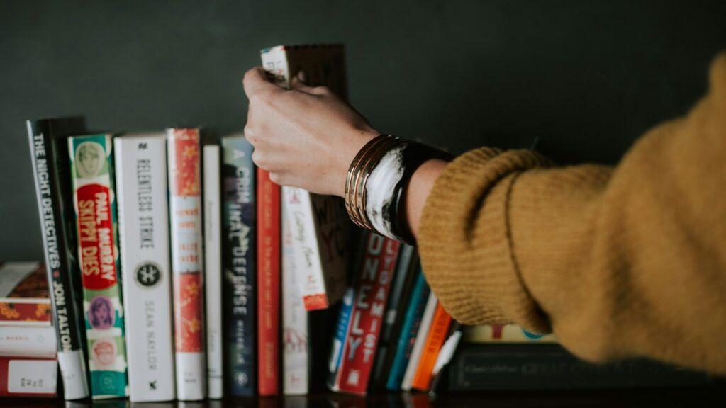 person picking white and red book on bookshelf